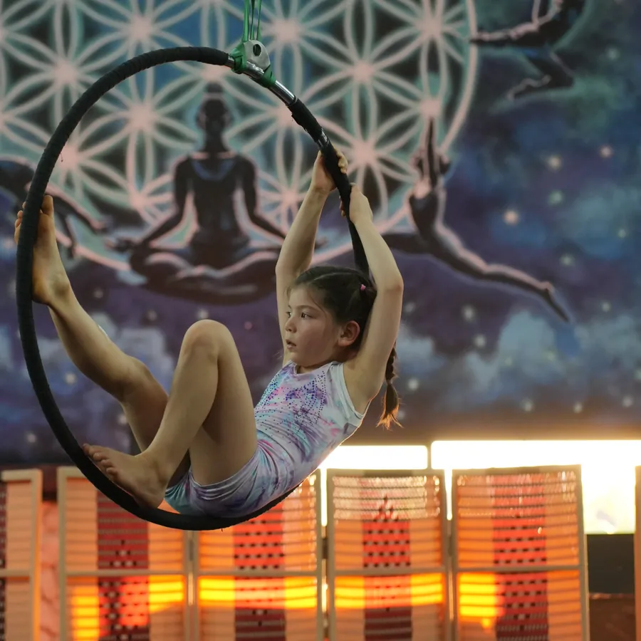 Kids aerial gymnastics class in Kerobokan, Bali — a young aerialist sitting into the hoop in front of the Flower of Life mural