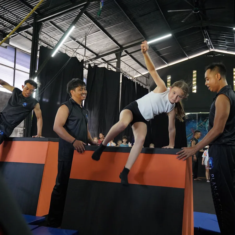 Kids parkour after-school class in Kerobokan, Bali — a girl clearing a vault box with two coaches spotting