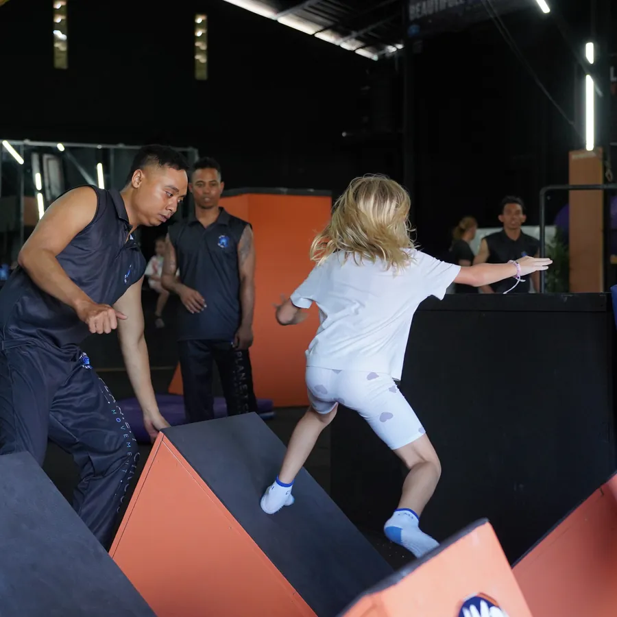Kids parkour weekend camp in Kerobokan, Bali — a child running across the obstacle blocks while a coach spots